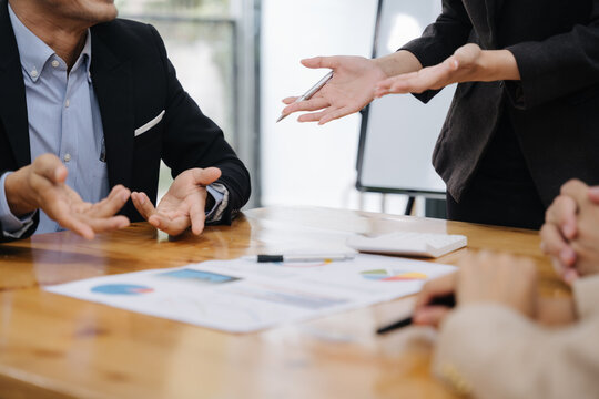 Business Collaboration at the Table: A focused team in sharp business attire, engaged in a dynamic business meeting, with hands gesticulating as ideas are shared over detailed documents.