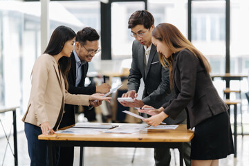 Collaborative Analysis: A team of focused business professionals huddles over documents and a...