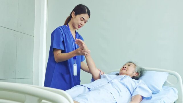 Female physiotherapist treats shoulder paralysis and arm numbness elderly woman lying on bed. Nurse treats pain by lifting right arm to treat muscle weakness in hospital.