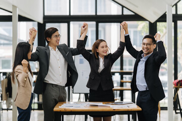 Business Success: A team of business professionals celebrates a victory, their hands raised high in...