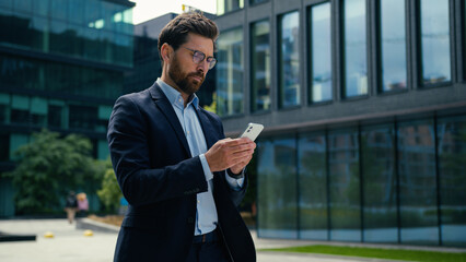Caucasian businessman man business guy male manager walking in city using mobile phone middle-aged employer entrepreneur working smartphone texting outdoors deal work job online internet scrolling