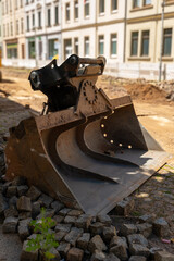 Excavator bucket resting on gravel during urban construction in bright daylight
