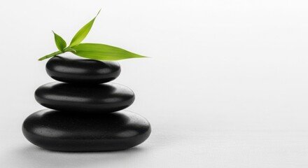 Obraz premium Stack of three black spa stones with a green bamboo leaf on top perfect for wellness and relaxation websites