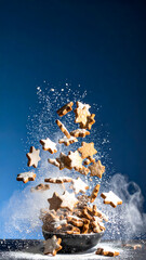 Star shaped cookies flying in air with flour particles against blue background, creating dynamic and festive scene