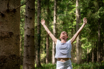 Woman practicing relaxation and mindfulness outdoors in a forest  with arms raised.
