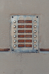 Wall-mounted intercom system displays multiple buttons for communication in a rustic urban setting