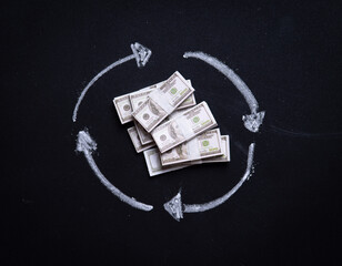 Rotating arrows drawn with bundles of money on a blackboard with white chalk to represent something cyclical,Financial Concept