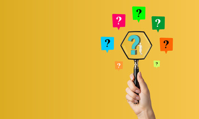 Hand Holding Magnifying Glass Over Hexagon Question Mark with Floating Colorful Query Symbols on Yellow Background - Concept of Search, FAQ, Problem Solving, and Inquiry