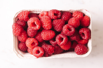 Fresh ripe raspberries in box. Sweet red berries in paper container. Healthy summer fruit. Organic...