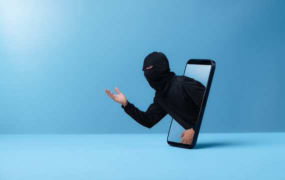 Criminal man wearing balaclava through smartphone on blue background,Theft of a smartphone, personal data.