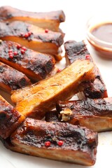 Delicious pork ribs and sauce on parchment paper, closeup