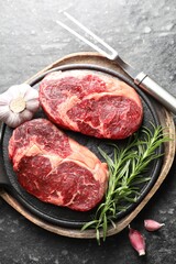 Pieces of raw beef meat, spices and carving fork on dark table, flat lay