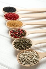 Different aromatic spices in spoons on white wooden table, closeup