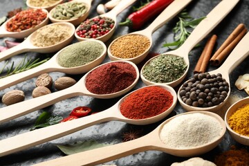 Many different spices in spoons on black table, closeup