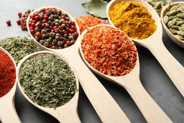 Many different spices in spoons on grey table, closeup