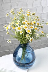 Beautiful chamomile flowers in vase on white table near grey wall