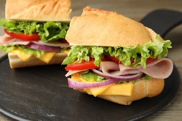 Pieces of tasty baguette sandwich with ham, cheese and vegetables on wooden table, closeup