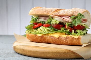 Tasty baguette sandwich with ham, cheese and vegetables on wooden table against grey background,...