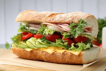 Tasty baguette sandwich with ham, cheese and vegetables on blurred grey background, closeup