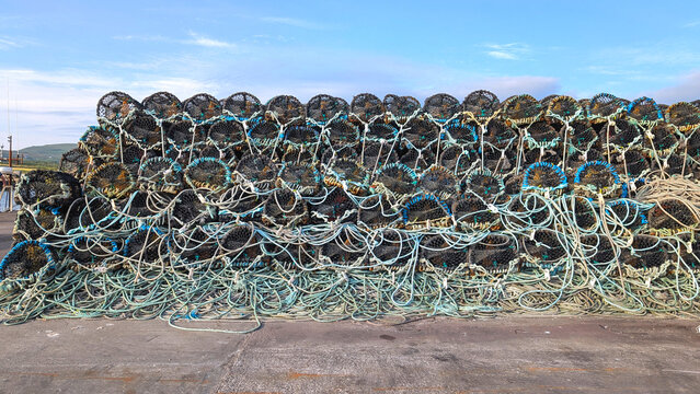 Big stack of Lobster traps arranged neatly on a coastal dock in a rural fishing village Portmagee in Ireland. Traditional fishing industry concept.