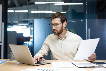 Focused young man financial specialist and analyst working in office with papers and documents,...