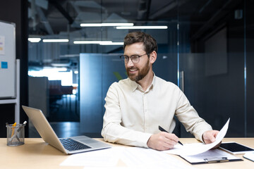 Smiling young businessman working in the office with documents, talking on a video call and holding an online conference with partners