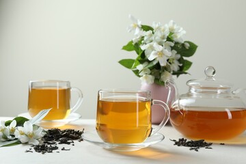 Aromatic jasmine tea in glass cups, teapot, flowers and dried leaves on white table