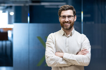 Portrait of a young programmer and engineer standing in the office with his arms crossed on his...