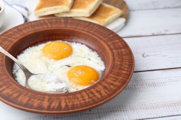 Half-boiled eggs in plate, spoon and toasted bread on white wooden table, closeup. Traditional asian breakfast