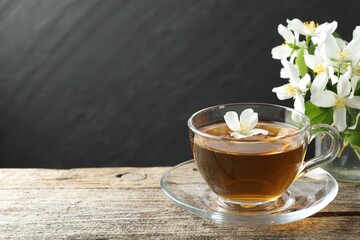 Aromatic jasmine tea in glass cup, flowers and green leaves on wooden table, closeup. Space for text