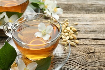 Aromatic jasmine tea in glass cups, brew and flowers on wooden table, closeup. Space for text