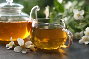 Tasty jasmine tea in cup, teapot and flowers on black table, closeup