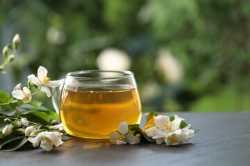 Tasty jasmine tea in cup and flowers on black table, closeup. Space for text