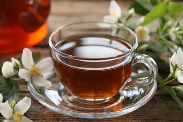 Tasty jasmine tea in cup and flowers on wooden table, closeup