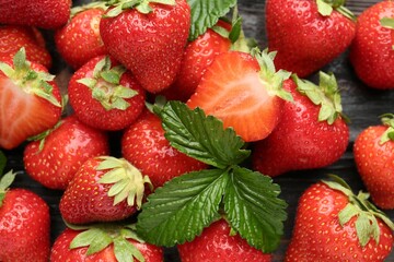 Fresh ripe strawberries and leaves on black wooden table, flat lay