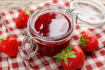 Tasty strawberry jam in glass jar and fresh berries on table, closeup