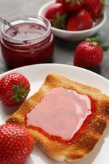 Toast with tasty homemade strawberry jam and berries on grey table, closeup