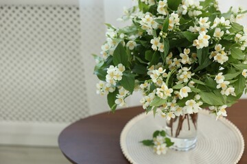 Beautiful jasmine flowers in vase on table indoors, closeup. Space for text
