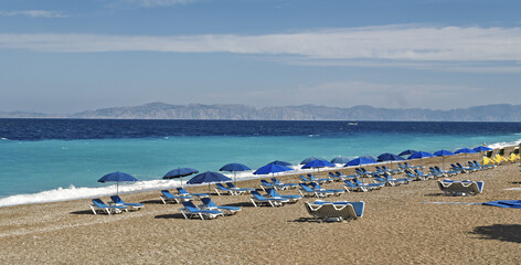 sand beach with blue deck chairs and umbrellas arranged in rows along the sea turquoise in Rhodes, Greece © hectorchristiaen