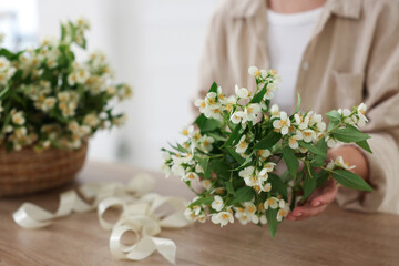 Woman making bouquet of jasmine branches at wooden table, closeup