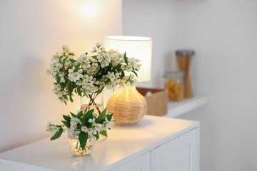 Bouquet of beautiful jasmine flowers in vase on white table indoors. Space for text