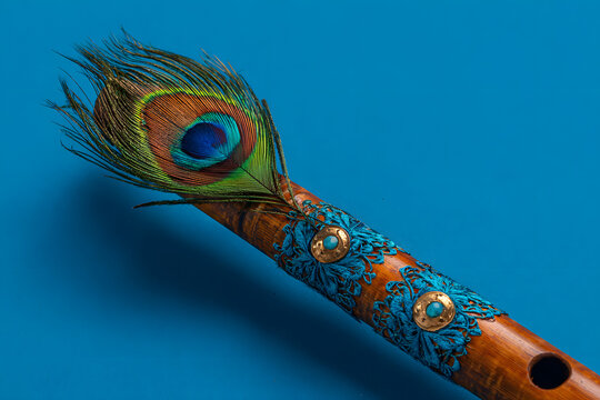 Bamboo flute decorated with peacock feather symbolic to hindu god lord krishna during celebration of janmashtami festival. photo taken in blue background with copy space.