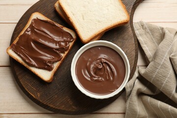 Tasty chocolate butter and slices of bread on light wooden table, top view