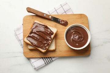 Tasty chocolate butter in bowl, slices of bread and knife on white marble table, top view