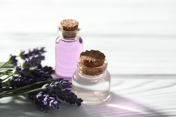 Natural essential oil and lavender flowers on white wooden table, closeup