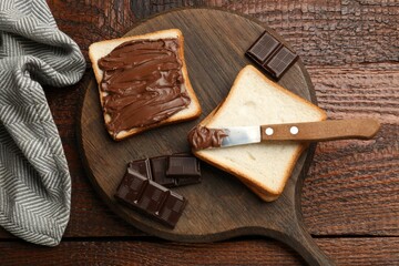 Tasty chocolate butter, pieces, knife and slices of bread on wooden table, top view