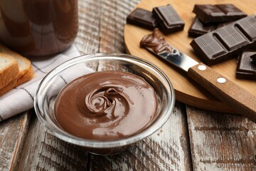 Tasty chocolate butter in glass bowl on color wooden table, closeup