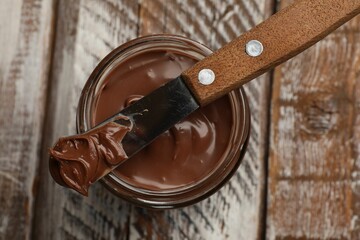 Tasty chocolate butter in glass jar and knife on color wooden table, top view