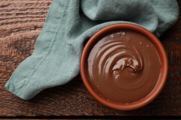 Tasty chocolate butter in bowl and napkin on wooden table, top view