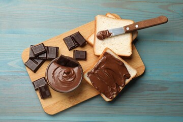 Tasty chocolate butter, pieces, knife and slices of bread on light blue wooden table, top view